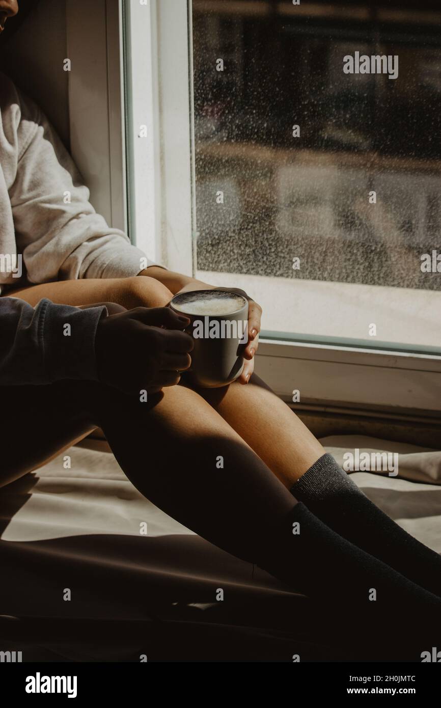 Une femme méconnaissable à la fenêtre de sa maison assise avec un latte de café chaud tout en appréciant le temps avec elle-même.Photographie de café STILL Life. Banque D'Images