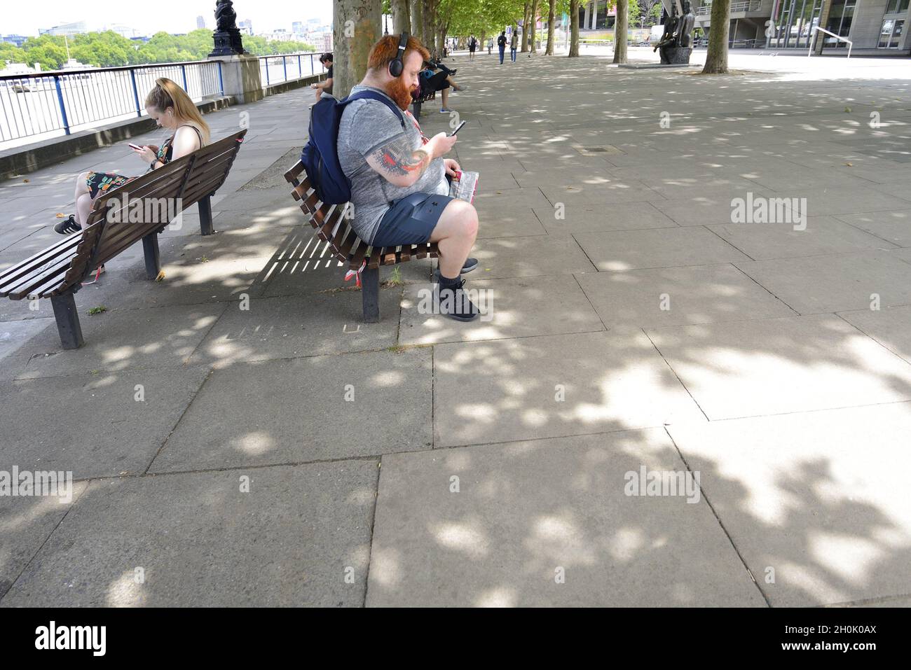 Londres, Angleterre, Royaume-Uni.Homme avec une barbe rouge brouillée, portant un short, regardant son téléphone mobile sur la rive sud Banque D'Images