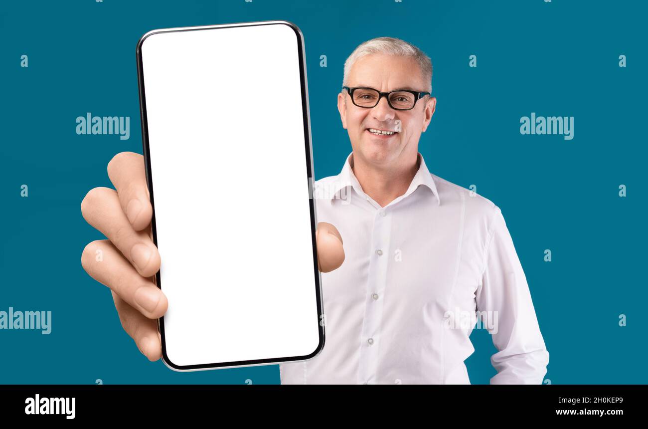 Excellente applicationHomme senior souriant montrant un smartphone avec écran vide sur l'appareil photo Banque D'Images