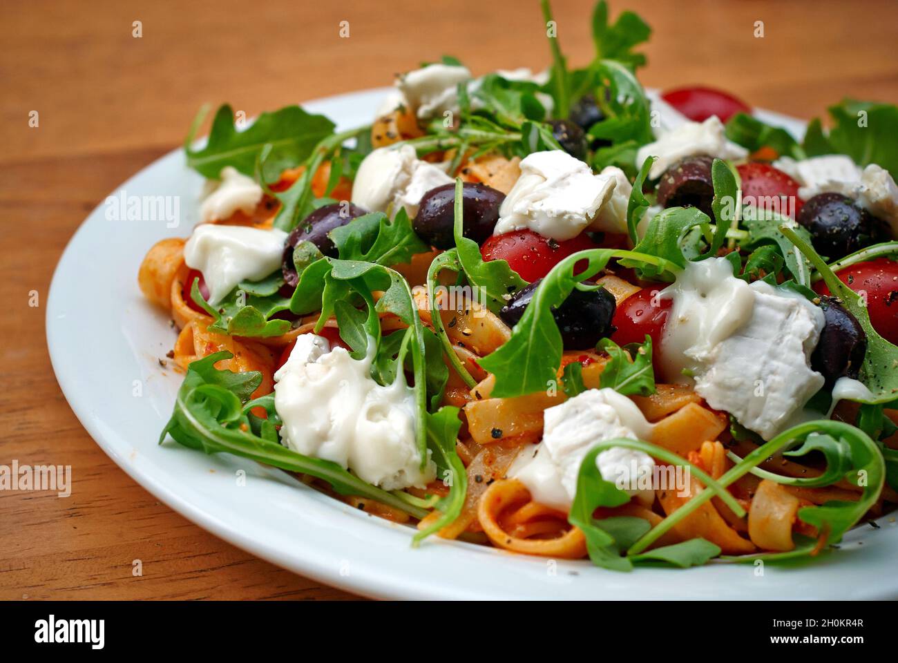 Plat de pâtes à tagliatelle avec olives, tomates, fromage de chèvre et feuilles de roquette. Banque D'Images