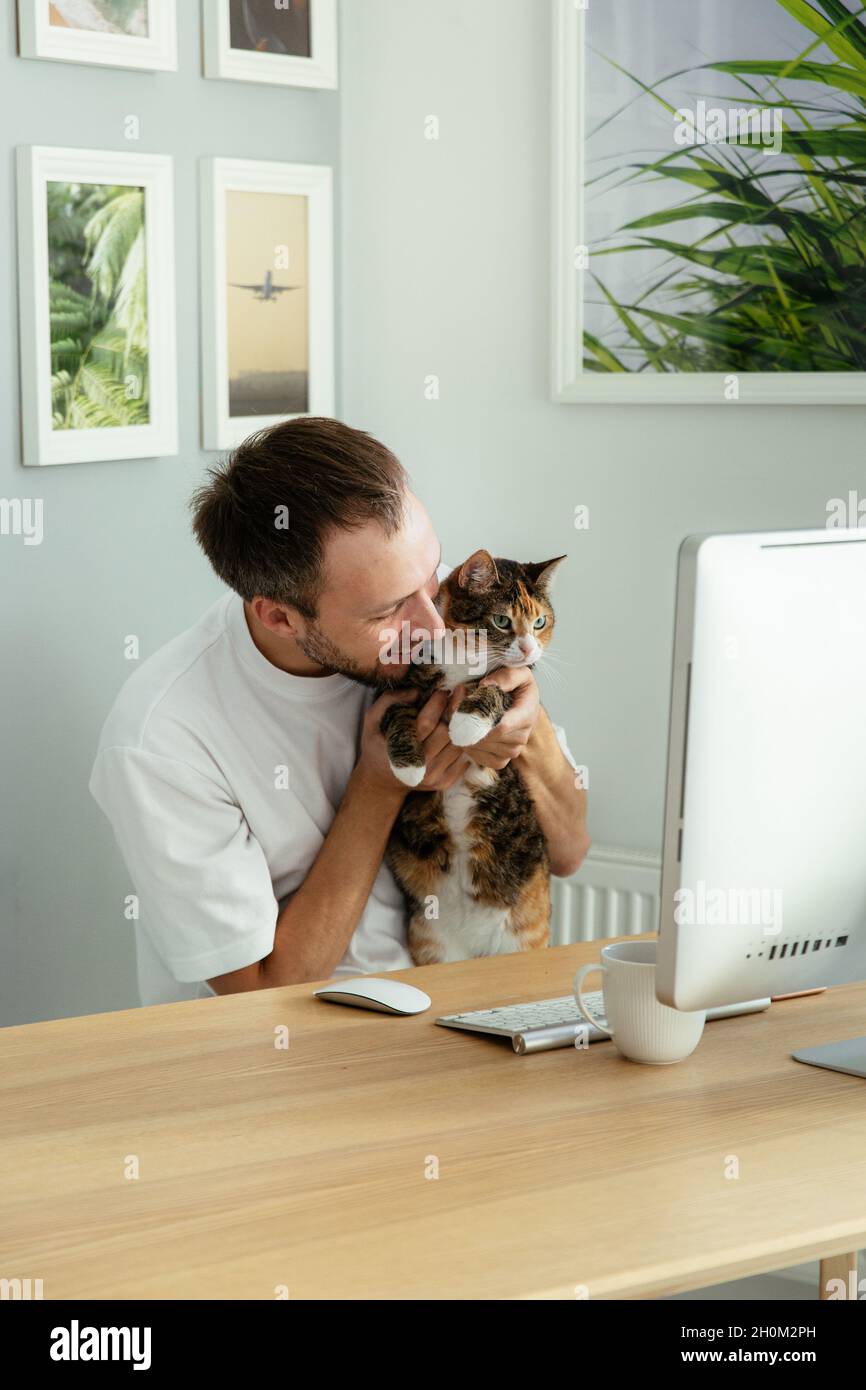 Heureux propriétaire d'animal de compagnie indépendant homme jouant avec le chat sur le lieu de travail comme soulagement de stress des problèmes au travail Banque D'Images