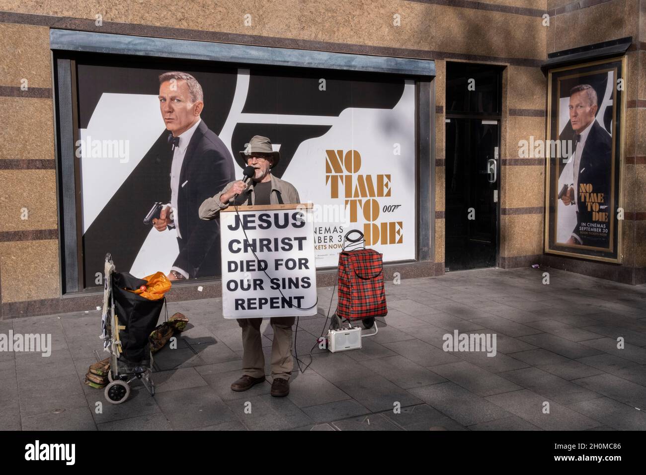 Un chrétien qui fréquente le West End et porte des messages religieux de la Bible, se dresse devant une affiche pour la dernière apparition de Daniel Craig en tant que James Bond dans le film « Not a Day to Die »,Qui s'est finalement ouvert dans tout le pays, retardé après la pandémie de Covid, le 12 octobre 2021, à Londres, en Angleterre. Banque D'Images