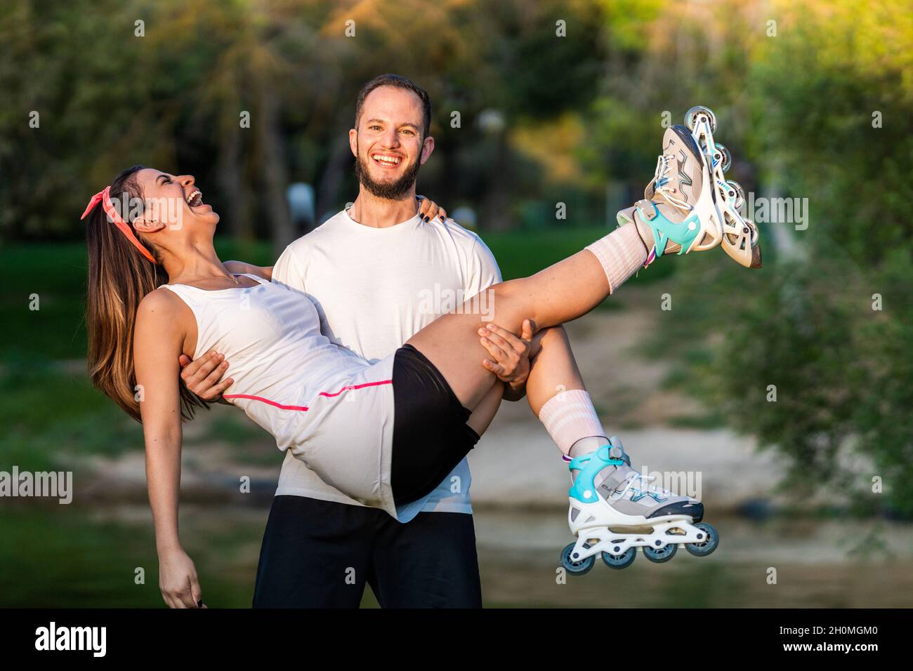 Homme tenant les bras une femme sur des patins à roues alignées dans un parc. Banque D'Images