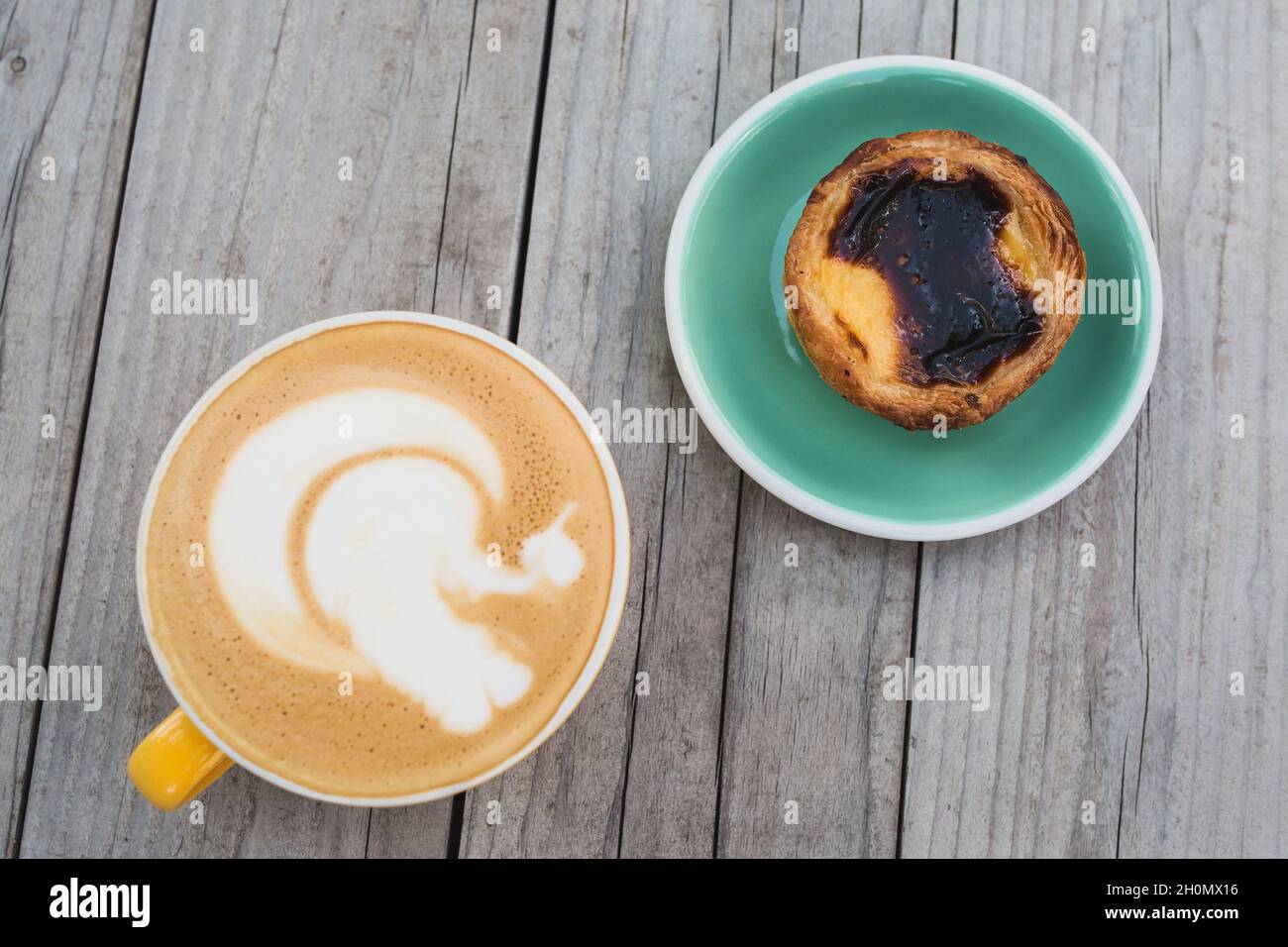 Vue de dessus d'une tasse de cappuccino et d'une assiette avec gâteau pastel de nata sur une table rustique en bois Banque D'Images