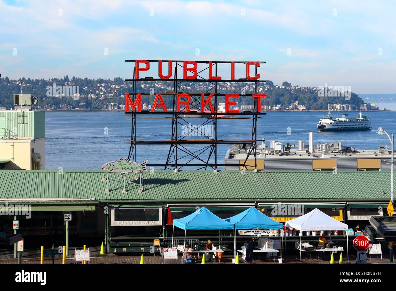 Vue sur le marché de Pike place et le panneau au néon du marché public avec Puget Sound, quartier du North Admiral et un Washington State Ferry en arrière-plan. Banque D'Images