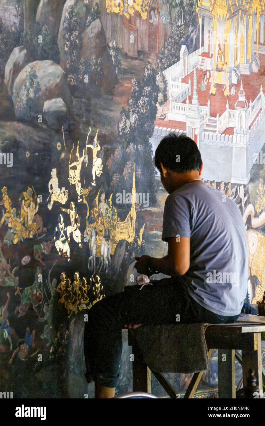 Un jeune artiste répare les dommages et la décoloration sur les peintures murales.Ramakien.Wat Phra Kaeo, Grand Palace, Bangkok, Thaïlande. Feuille d'or, dorure. Banque D'Images