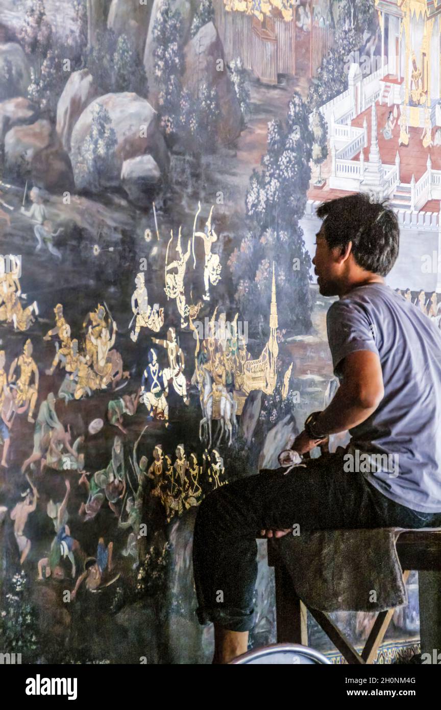 Un jeune artiste répare les dommages et la décoloration sur les peintures murales.Ramakien.Wat Phra Kaeo, Grand Palace, Bangkok, Thaïlande. Feuille d'or, dorure. Banque D'Images