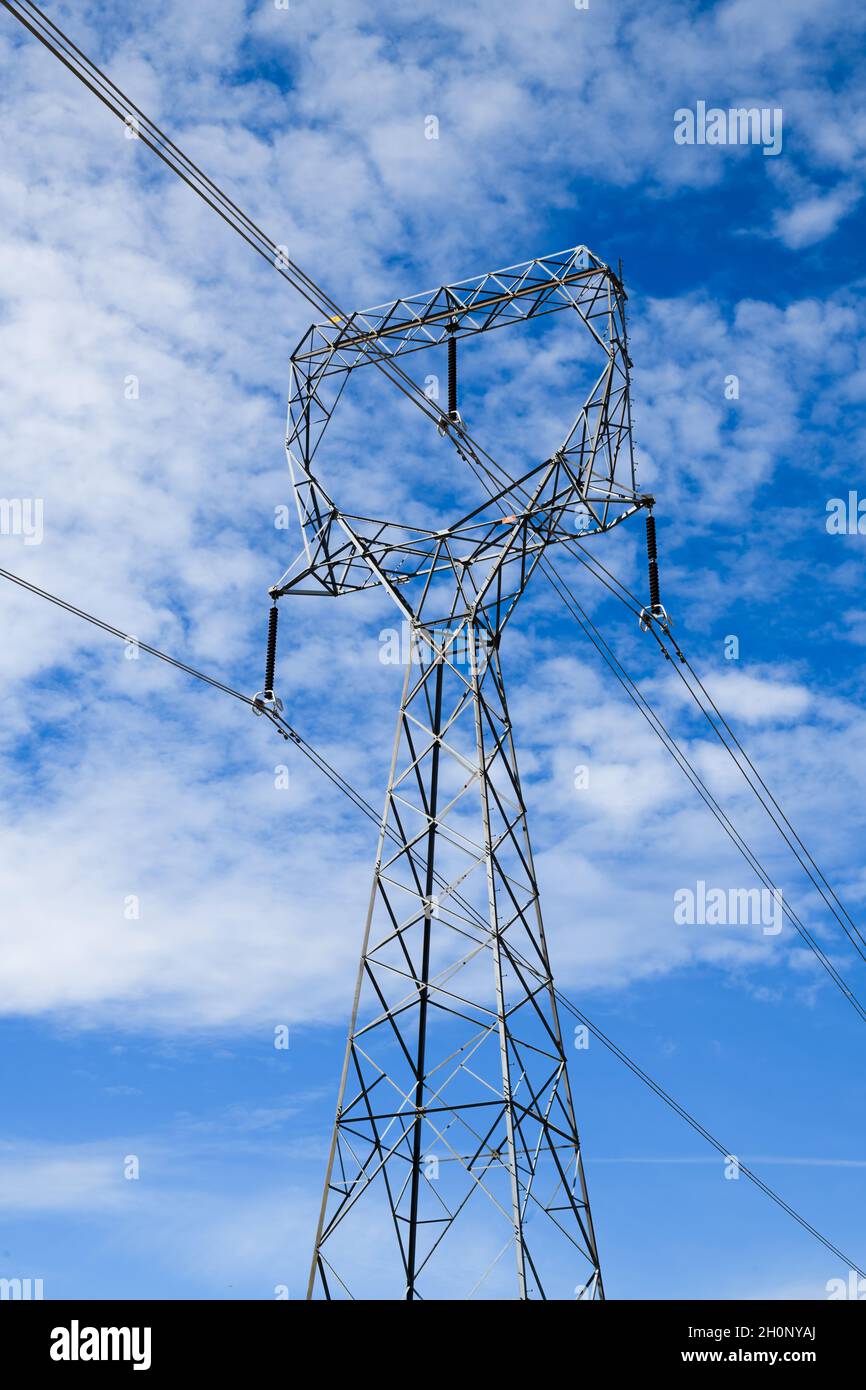 Une tour de transmission haute tension est montée contre un ciel bleu parsemé de nuages blancs par une journée ensoleillée.Les fils pendent des isolateurs Banque D'Images