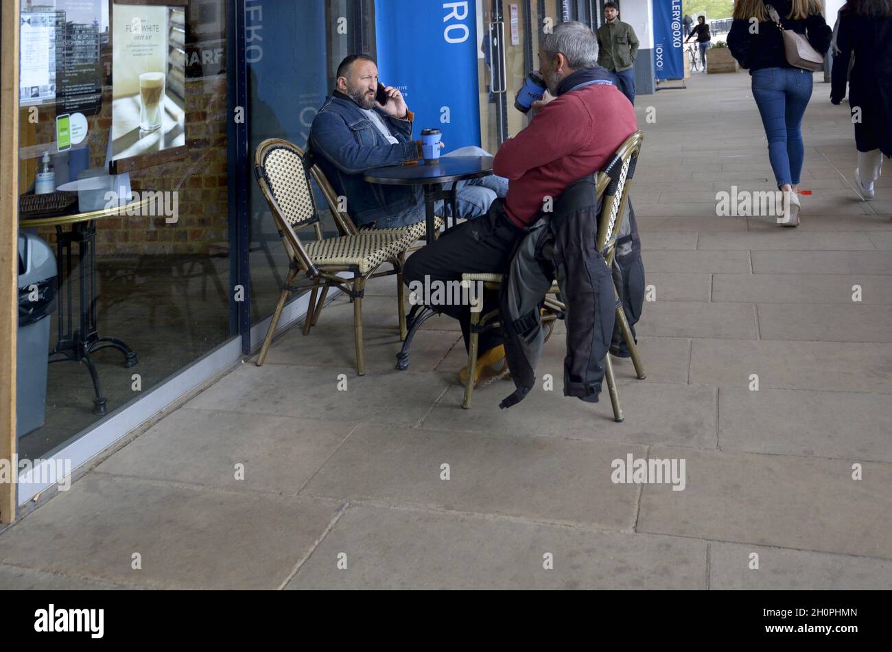 Londres, Angleterre, Royaume-Uni.Des hommes assis à l'extérieur d'un café avec un café et un téléphone portable Banque D'Images