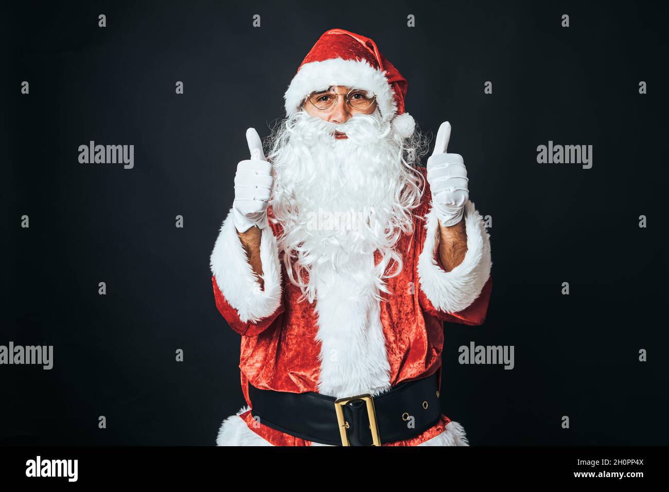 Homme habillé comme le Père Noël avec les pouces vers le haut, sur fond noir.Concept de Noël, Père Noël, cadeaux, fête. Banque D'Images