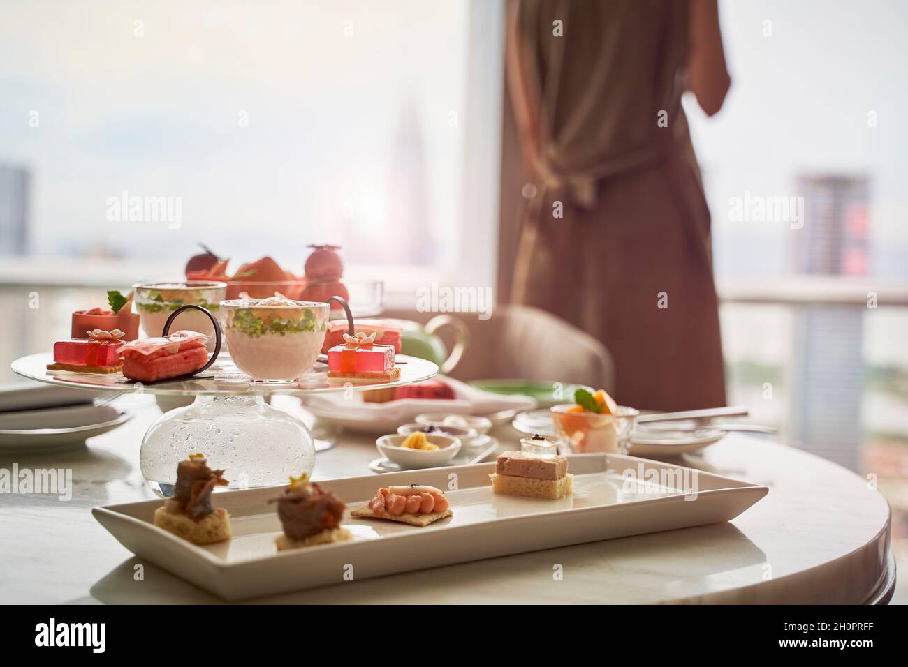 femme asiatique mûre, debout près de la fenêtre, avec vue sur la ville et repas sur table dans une chambre d'hôtel Banque D'Images