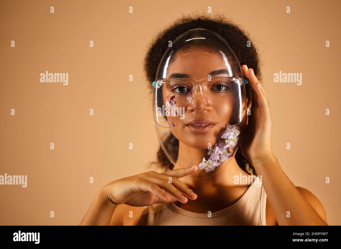 Jeune femme afro-américaine gaie portant un masque de protection en PVC transparent orné de fleurs et regardant la caméra avec beaming sm Banque D'Images