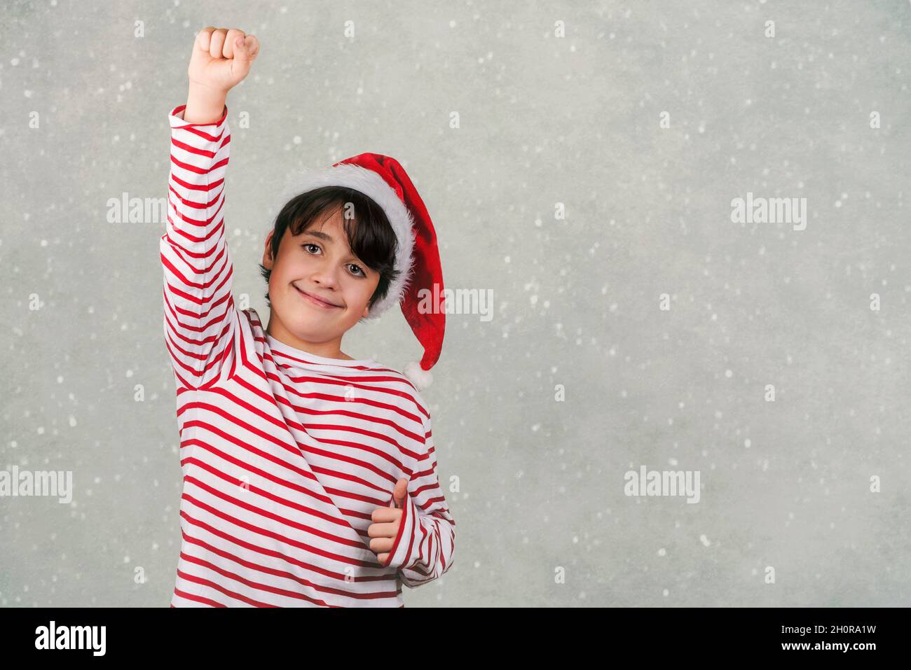 Joyeux Noël.enfant souriant portant le chapeau du Père Noël sur fond gris neige Banque D'Images