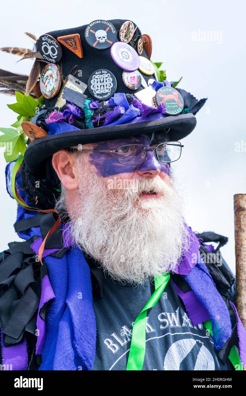 Visage d'un homme mûr avec une barbe blanche, portant des lunettes et un chapeau noir orné de badges, membre des Black Swan Border Morris Dancers. Banque D'Images