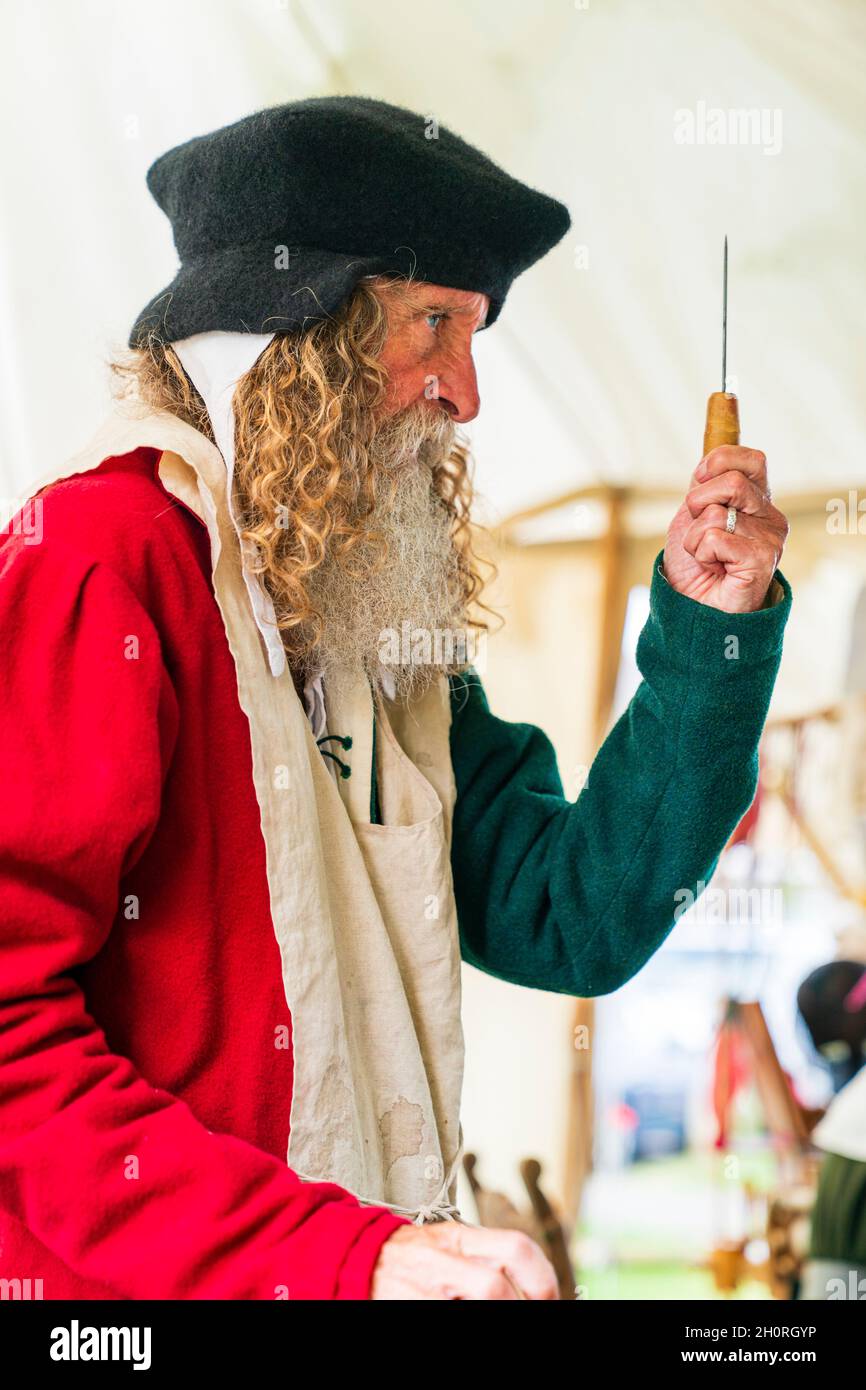 Reconstitution médiévale, vue latérale d'un homme âgé, avec une barbe complète, montre à une personne invisible, l'un de ses outils chirurgicaux debout. Banque D'Images