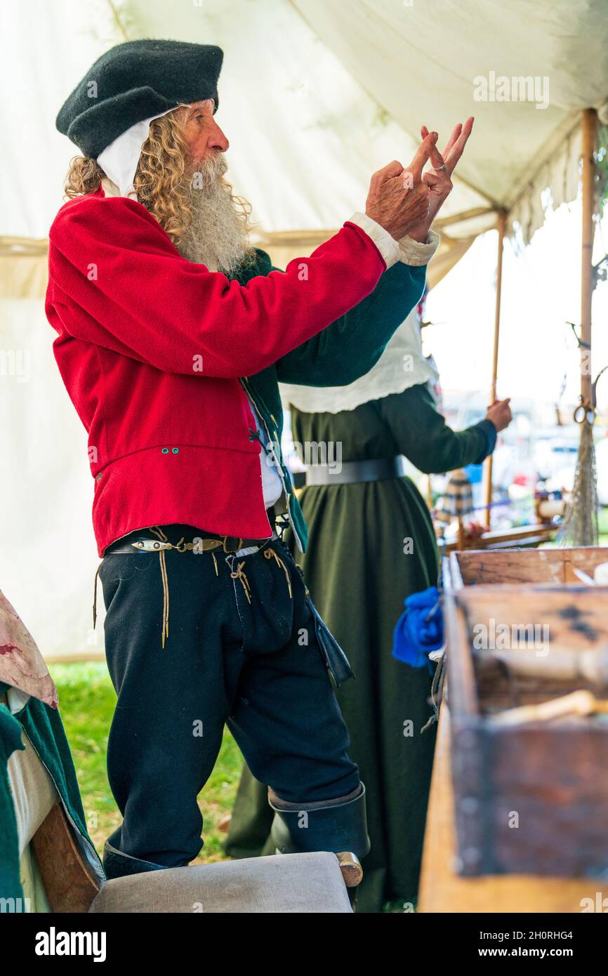 Reconstitution médiévale, vue latérale d'un homme âgé, avec une barbe complète, parlant à une personne non vue, et utilisant ses mains pour représenter les nombres en position debout. Banque D'Images