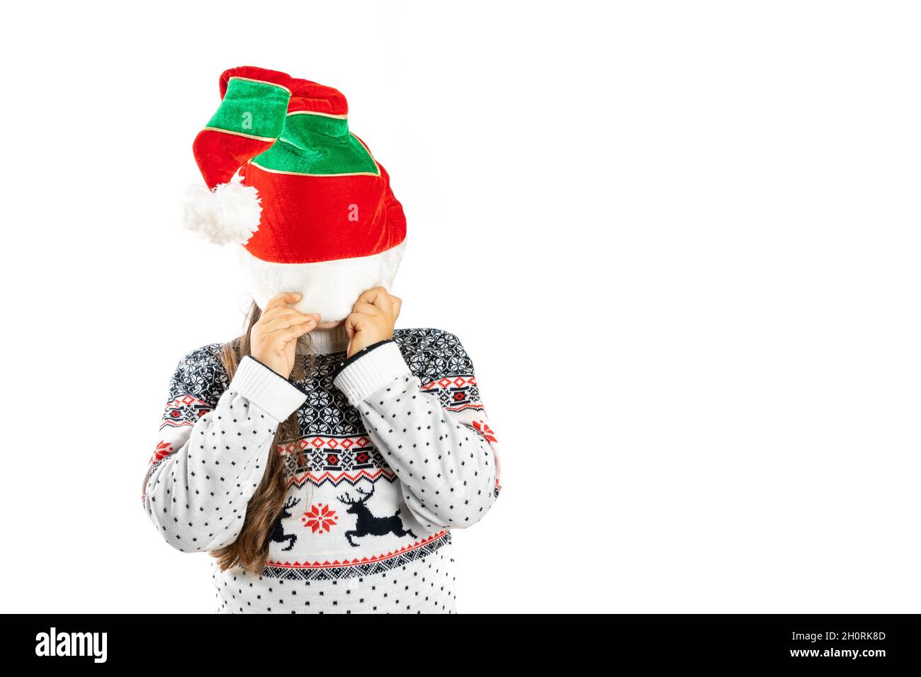 Enfant en tricot blanc chandail de Noël avec renne cache face sous un chapeau nain, isolé sur fond blanc Banque D'Images