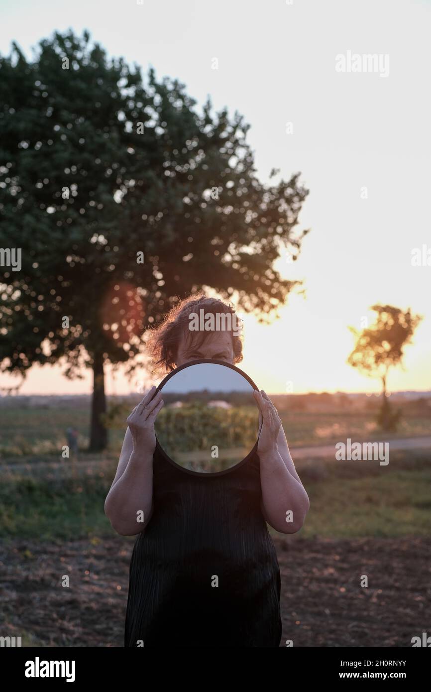 Portrait d'une femme debout dans un champ tenant un miroir devant son visage, France Banque D'Images