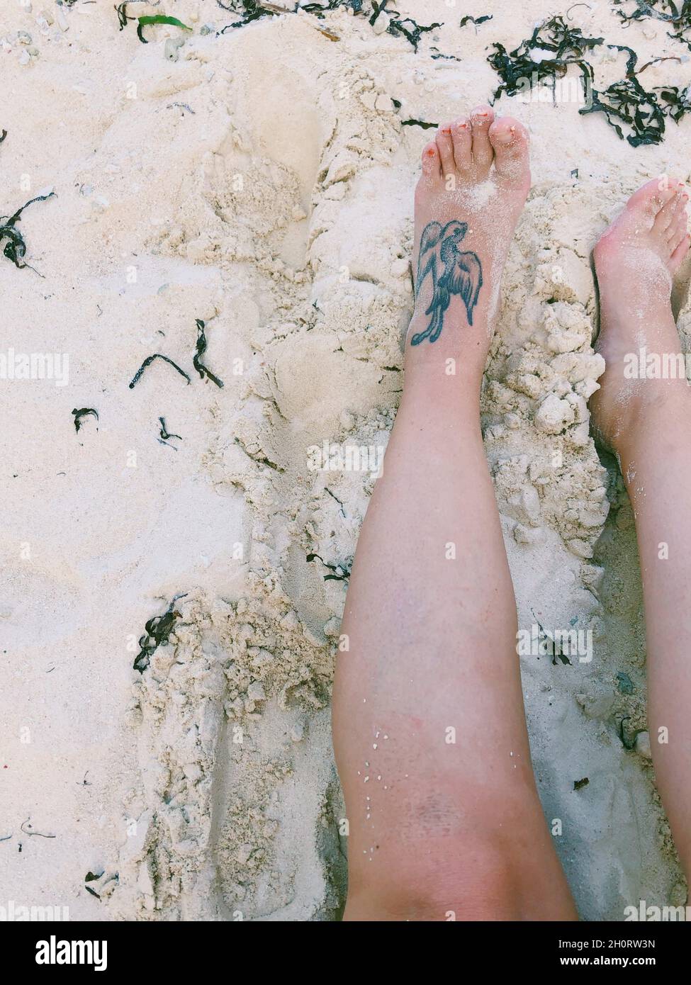 Vue en hauteur des jambes d'une femme avec un tatouage pour hirondelles sur une plage de sable, Philippines Banque D'Images
