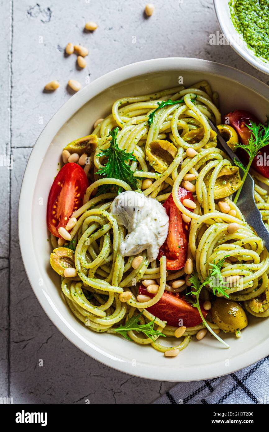 Pâtes spaghetti à la sauce pesto, olives, tomates et pignons dans un bol blanc.Concept de cuisine italienne. Banque D'Images