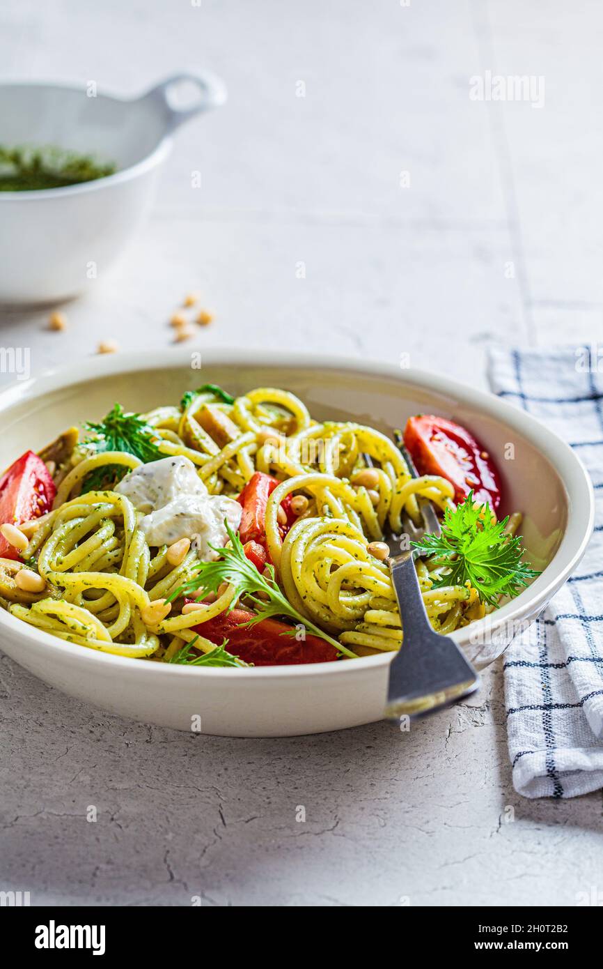 Pâtes spaghetti à la sauce pesto, olives, tomates et pignons dans un bol blanc.Concept de cuisine italienne. Banque D'Images