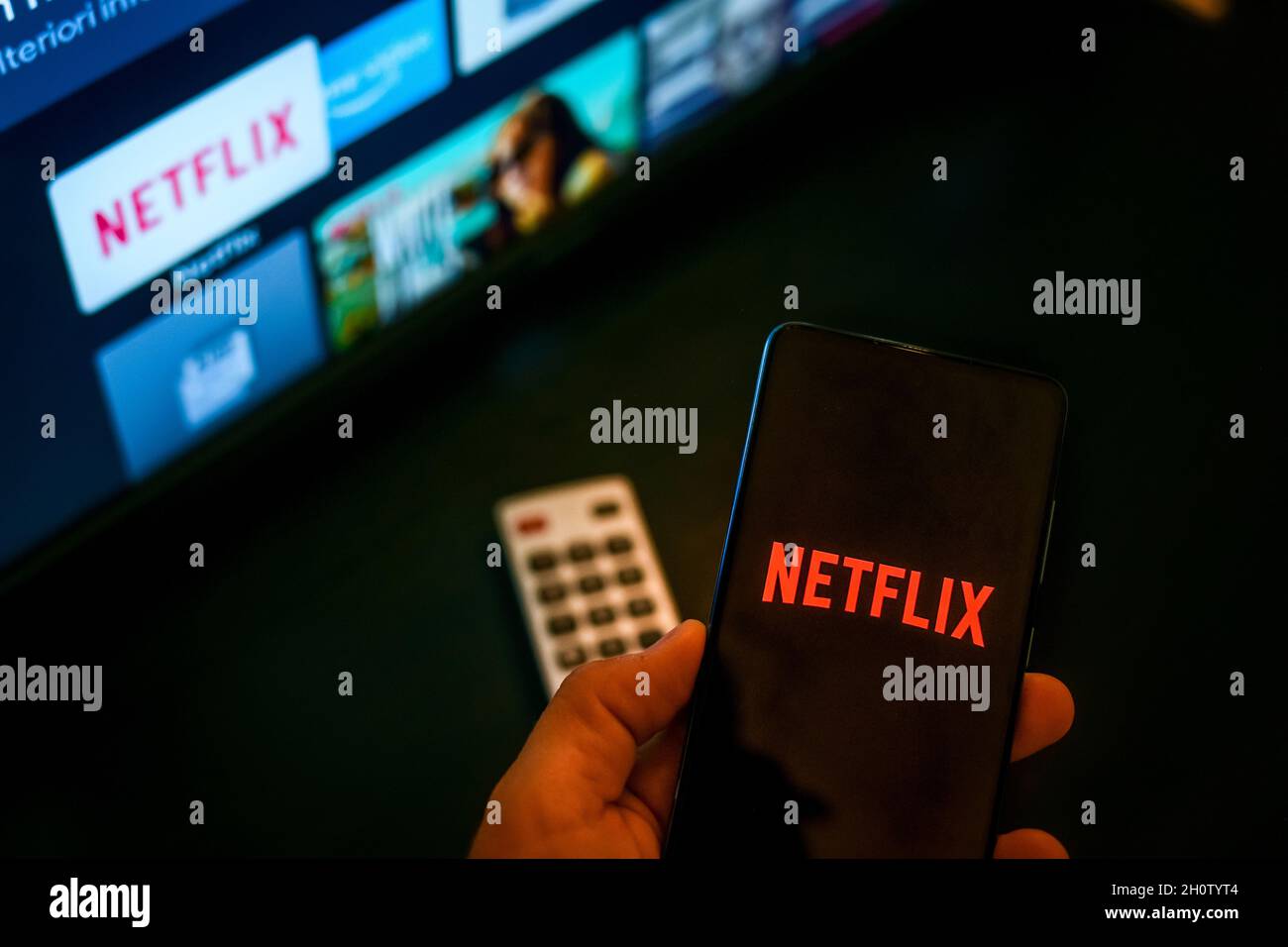 Vue rapprochée de la main avec le smartphone et Netflix ​logo à l'écran.Télévision en arrière-plan.Nouvelle technologie, série, réseau, film, cinéma,comédie, e Banque D'Images