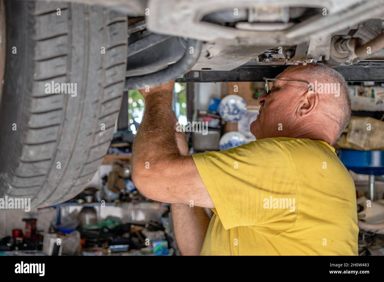 Un mécanicien de voiture expérimenté vérifie et répare une voiture soulevée dans son garage.Contrôle des freins.Vieux concept de mécanique et de réparation de voiture. Banque D'Images