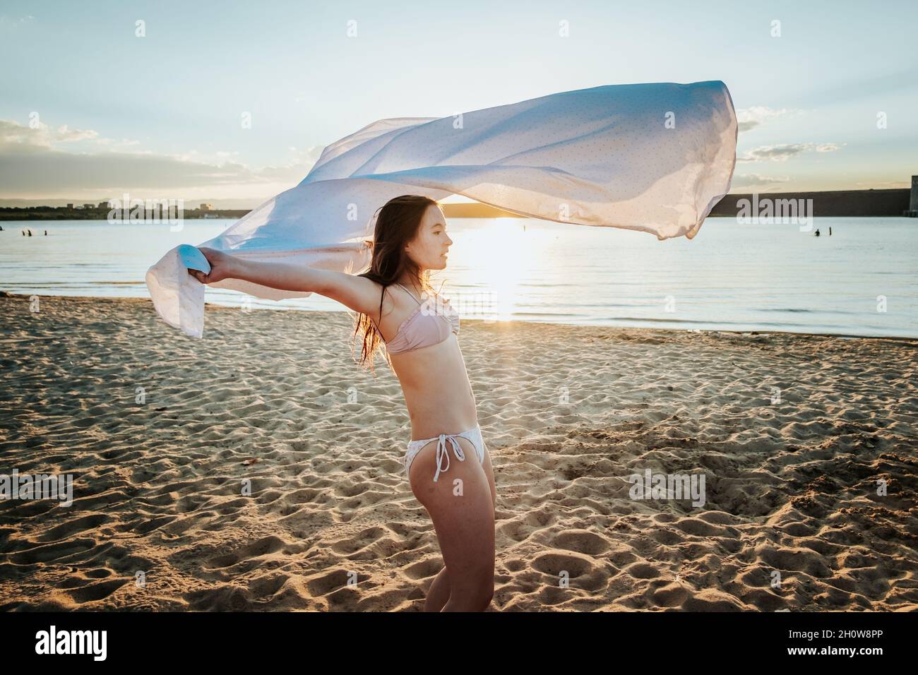Une jeune fille enveloppe la feuille autour d'elle sur la plage au coucher du soleil Banque D'Images
