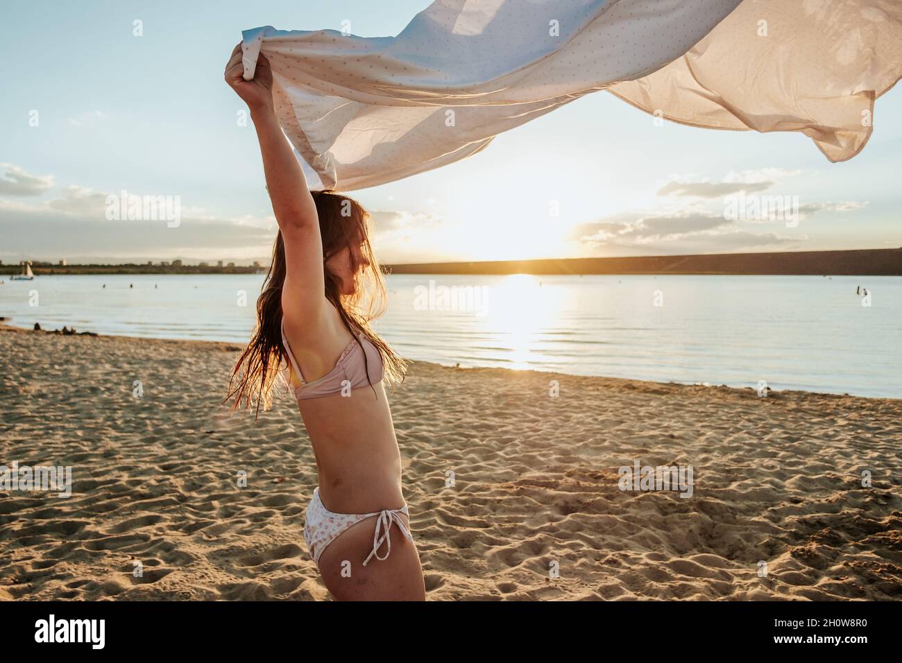 Jeune fille jouant avec la feuille blanche au coucher du soleil sur la plage Banque D'Images