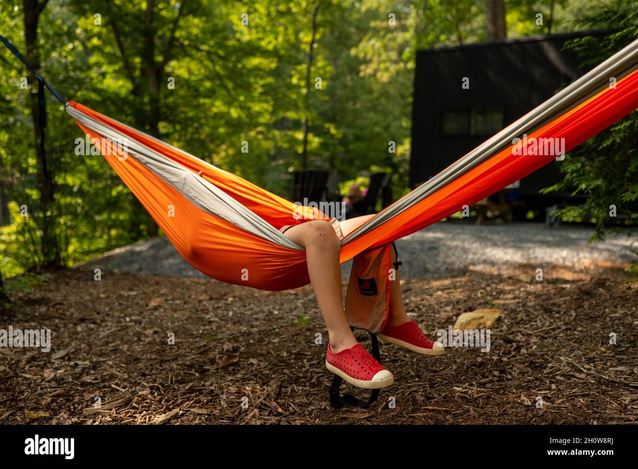 Jambes d'un petit garçon suspendu d'un hamac orange dans un camping Banque D'Images