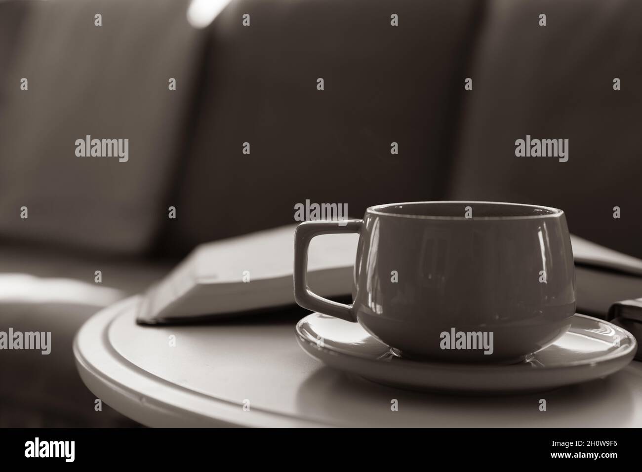 café sur une soucoupe sur une table ronde blanche avec livre ouvert, bible, devant un canapé en cuir Banque D'Images
