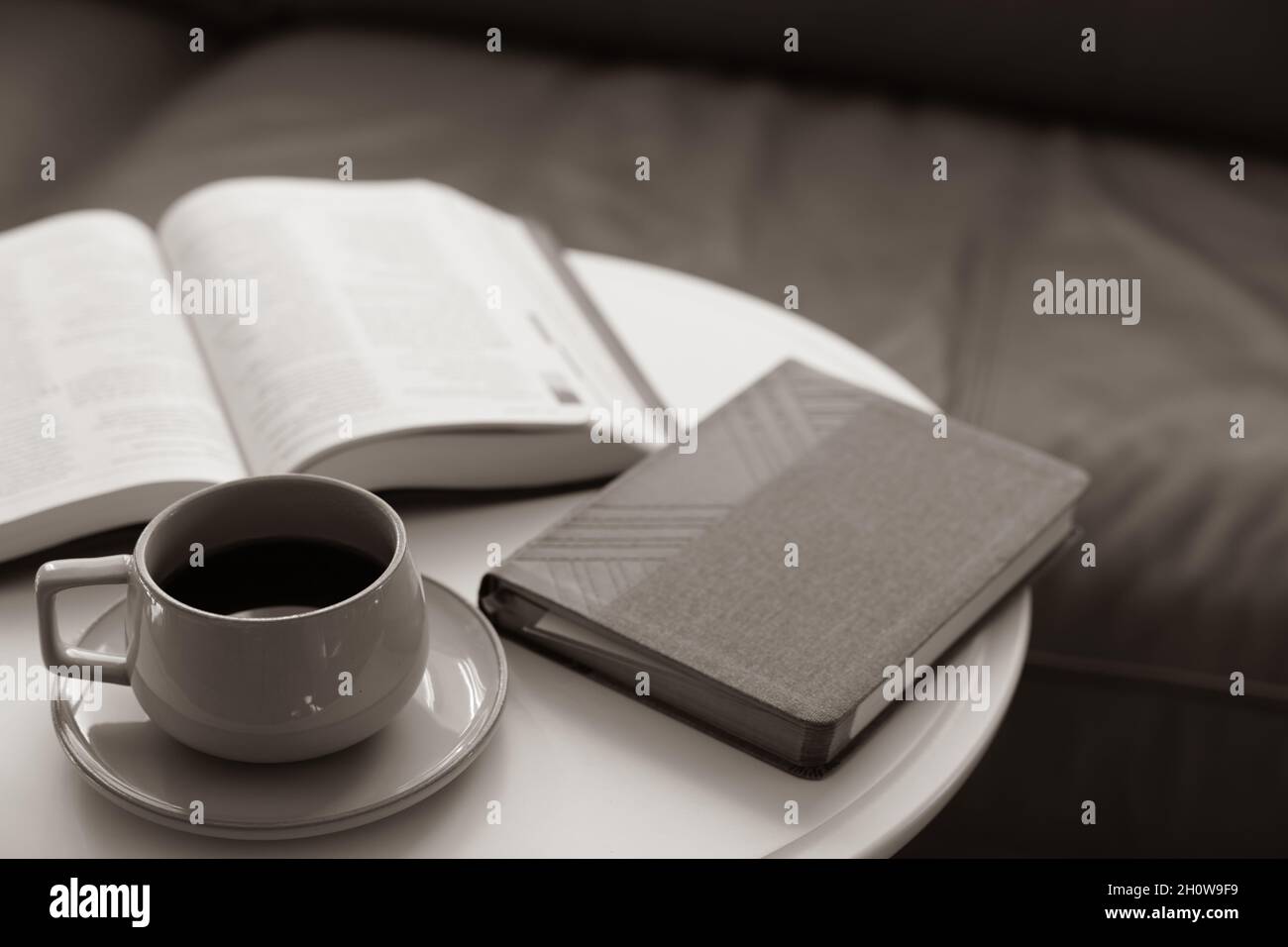 café sur une soucoupe sur une table ronde blanche avec livre ouvert, bible, devant un canapé en cuir Banque D'Images