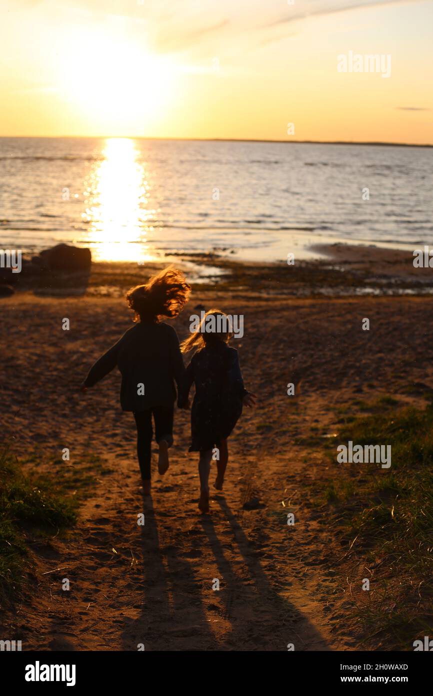 Deux filles courent à la mer au coucher du soleil. Banque D'Images