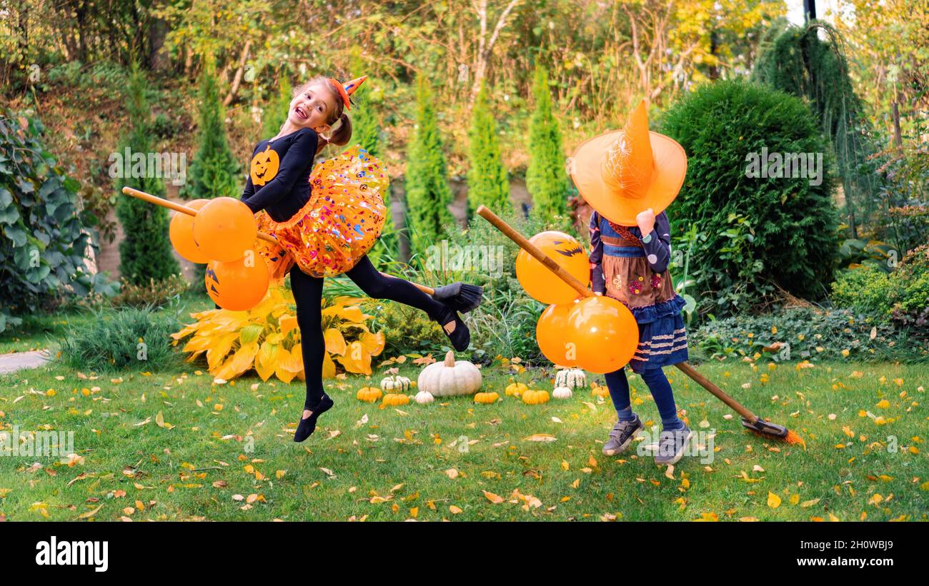 Petite sorcière volant sur un bâton de couvée sur Halloween.deux filles dans un costume de sorcière apprennent à voler sur un balai sautant dans l'air.Enfants en carnaval Banque D'Images
