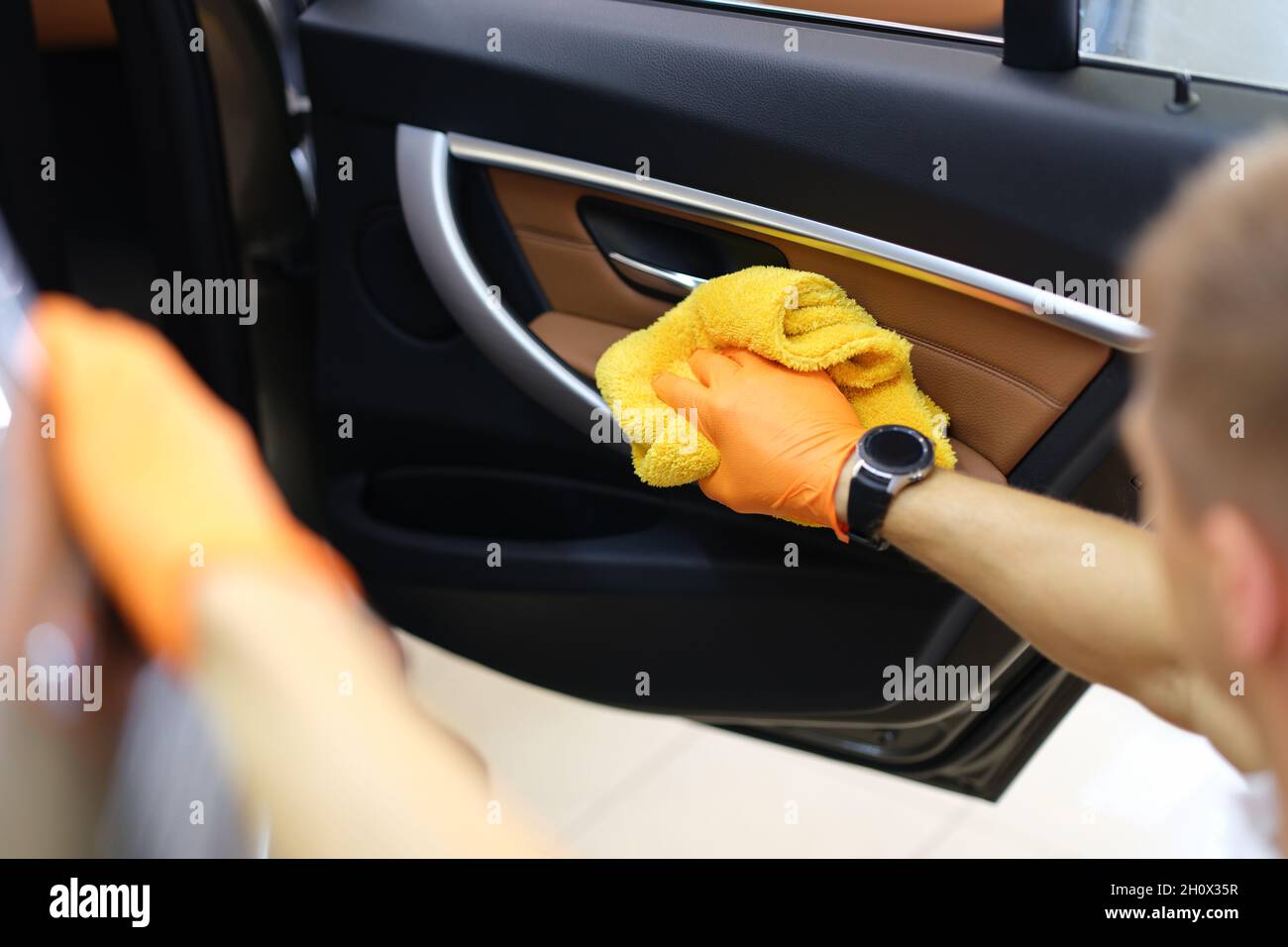 Un homme de main ganté essuie les portes de voiture à l'intérieur de la cabine Banque D'Images