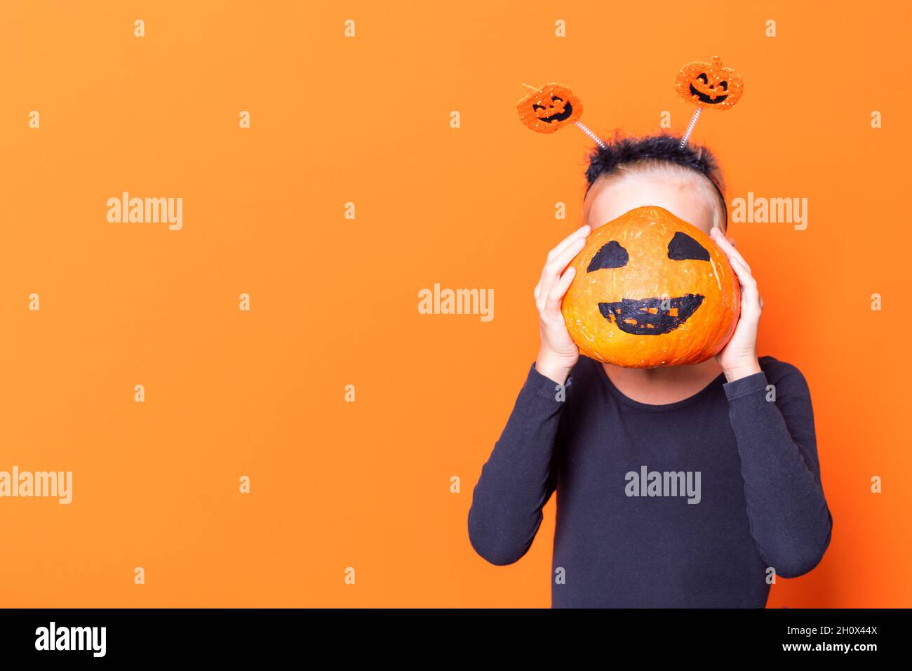 Halloween enfants.Une fille tenant une citrouille devant son visage avec un visage peint et créepy sur un fond orange, espace de copie.Ambiance de la saison d'Halloween.H Banque D'Images