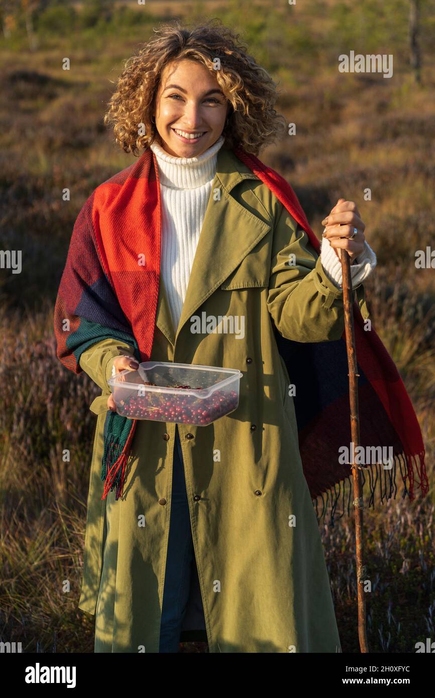 Activité de loisirs dans la nature : jeune femme heureuse cueillant des canneberges marchant dans des bois d'automne sur des marécages Banque D'Images