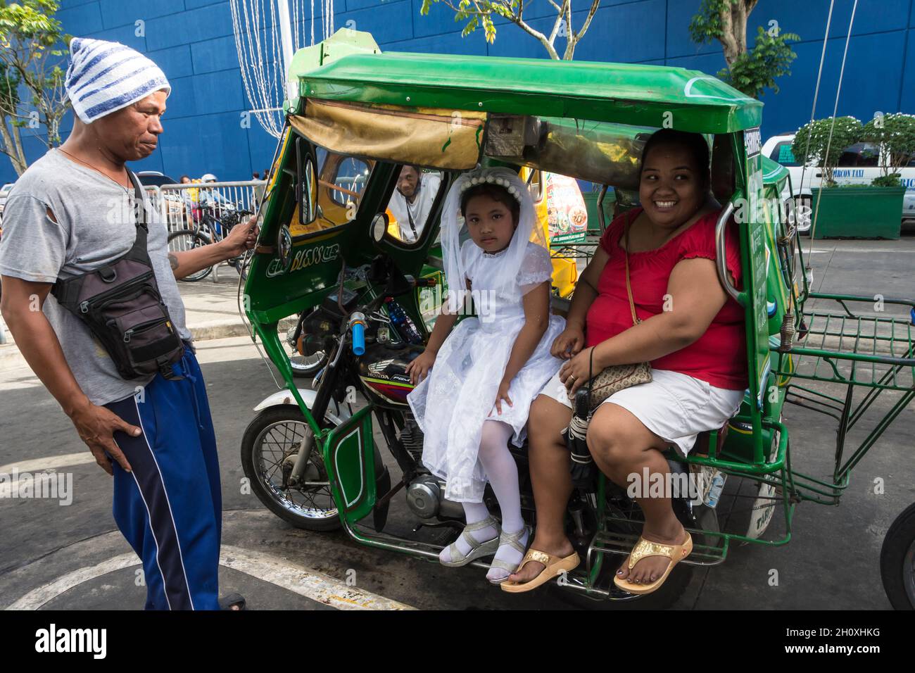 Fille en robe de communion blanche se trouve à côté de sa mère dans un taxi automobile philippin à Naga, région de Bicol, Philippines Banque D'Images