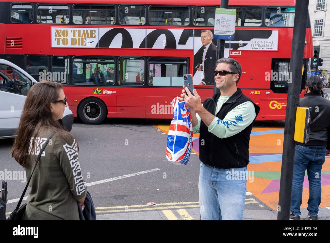 Alors qu'un bus passe devant le mariage d'un panneau publicitaire pour le dernier James Bond « No Time to Die » avec Danial Craig, un visiteur du West End prend une photo d'une femme, le 14 octobre 2021, à Westminster, Londres,Angleterre. Banque D'Images