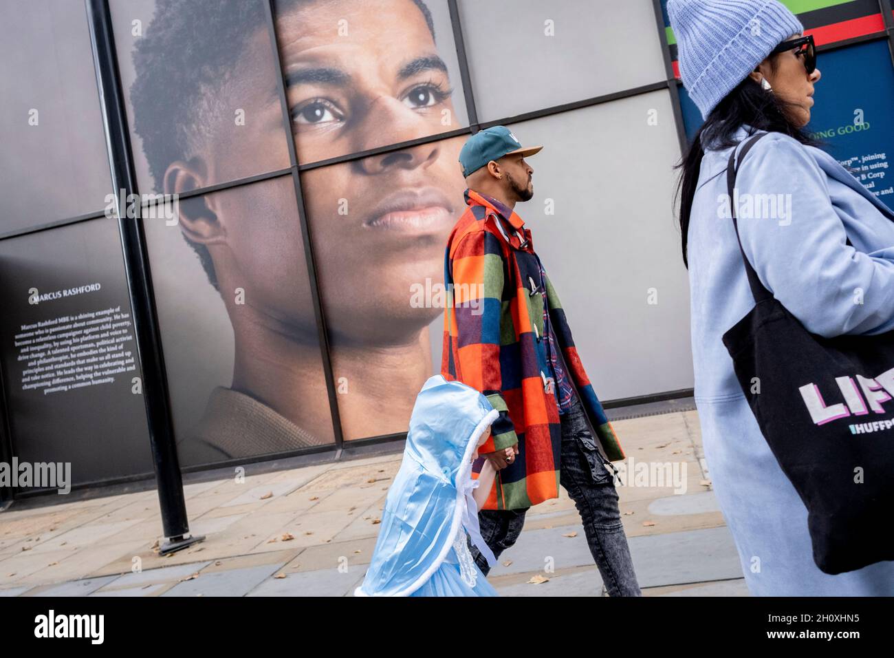 Un enfant et un adulte marchent sous le grand panneau d'affichage, un portrait du joueur de football anglais, Marcus Rashford, à l'extérieur de la branche Strand de Coutts Bank, le 14 octobre 2021, à Westminster, Londres,Angleterre.Marcus Rashford a récemment reçu un diplôme honorifique de l'Université de Manchester en reconnaissance de sa campagne politique au nom des personnes défavorisées (en particulier, des repas scolaires) et de sa philanthropie.Il joue actuellement pour Manchester United et fait partie de l'équipe nationale anglaise.Il a également été victime d'abus racial en ligne. Banque D'Images