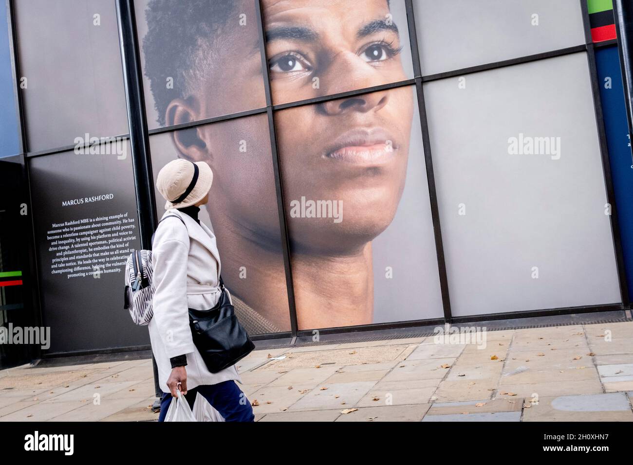 Une femme de couleur marche sous le grand panneau d'affichage, un portrait du joueur de football anglais, Marcus Rashford, outside la branche Strand de Coutts Bank, le 14 octobre 2021, à Westminster, Londres,Angleterre.Marcus Rashford a récemment reçu un diplôme honorifique de l'Université de Manchester en reconnaissance de sa campagne politique au nom des personnes défavorisées (en particulier, des repas scolaires) et de sa philanthropie.Il joue actuellement pour Manchester United et fait partie de l'équipe nationale anglaise.Il a également été victime d'abus racial en ligne. Banque D'Images