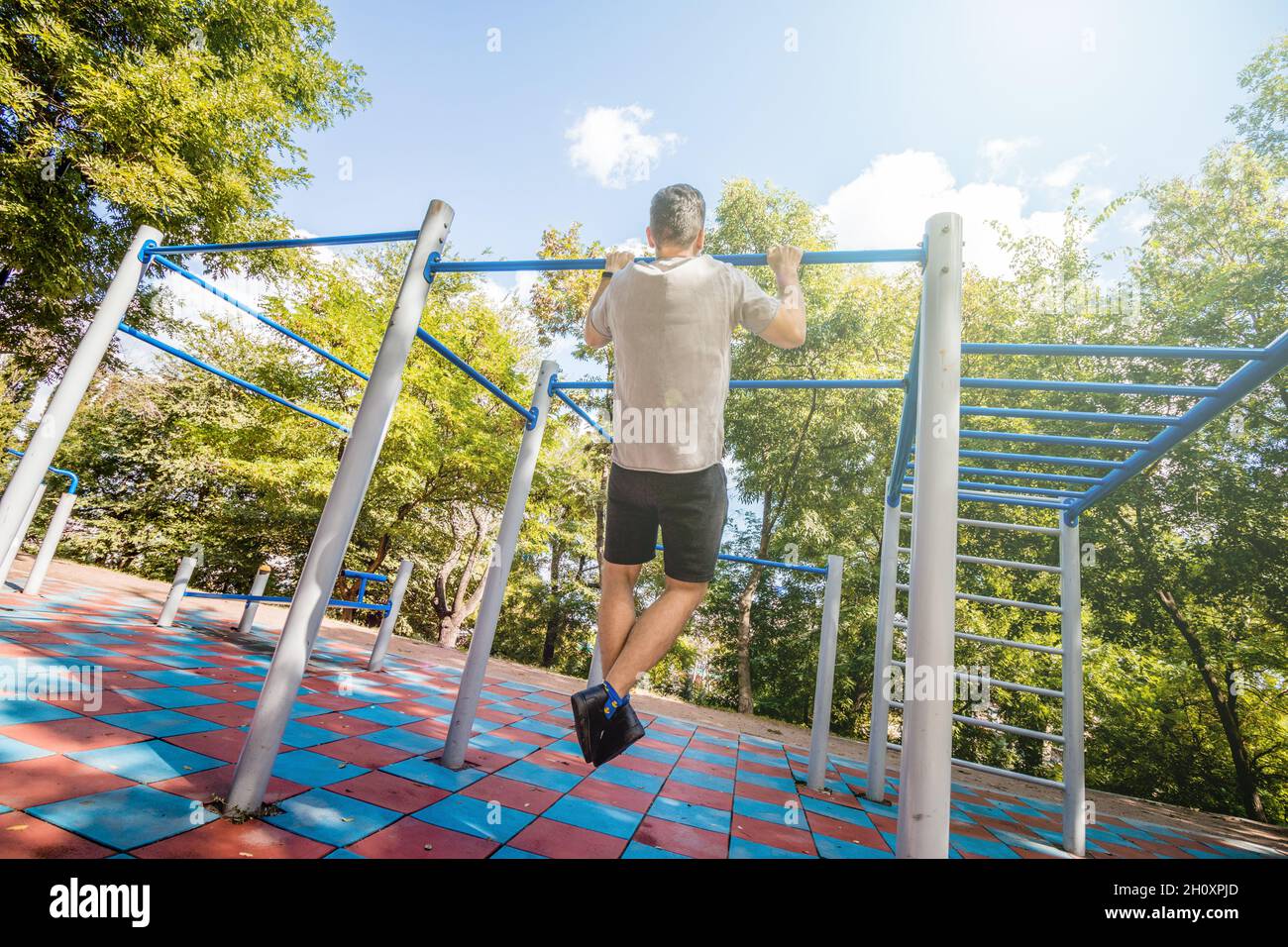 Un homme qui fait des pull-ups sur une barre horizontale sur une aire de jeux par une journée ensoleillée. Banque D'Images