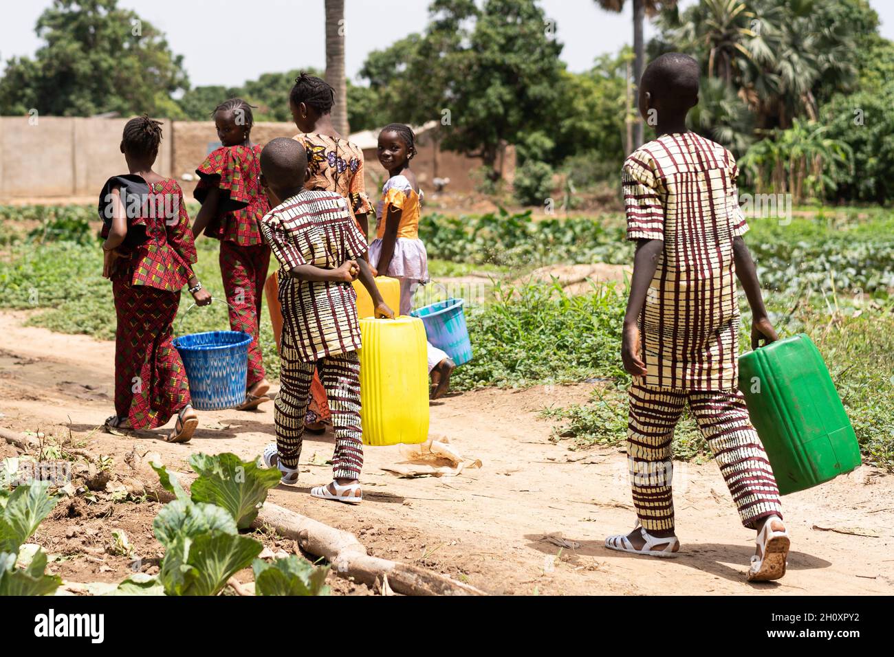 Groupe d'enfants africains noirs transportant des conteneurs d'eau vides sur leur chemin de retour du village bien après avoir aidé à arroser les champs de houles Banque D'Images