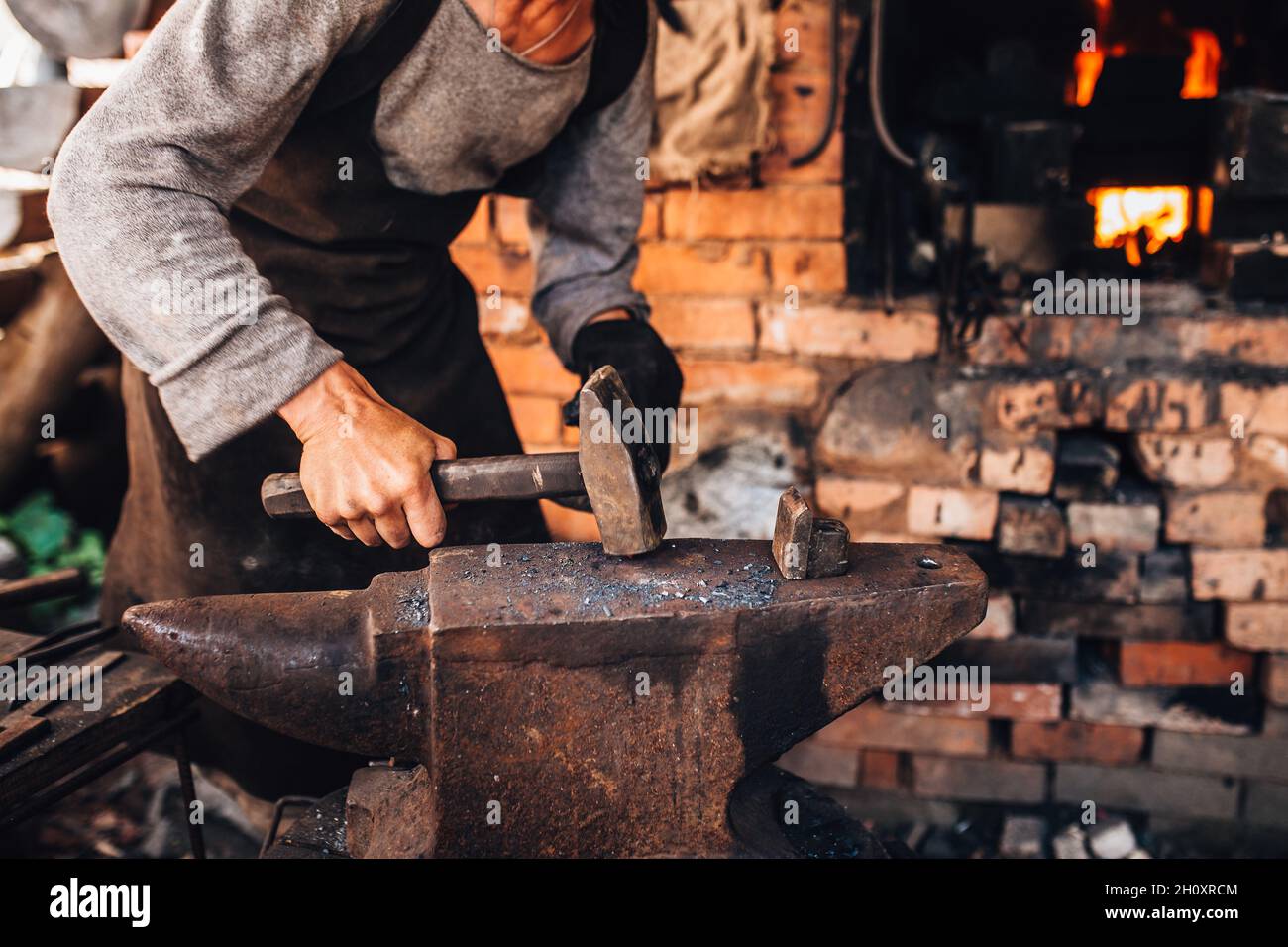 Un forgeron mâle forge à la main dans une forge sur une enclume en acier - un vieux métier Banque D'Images