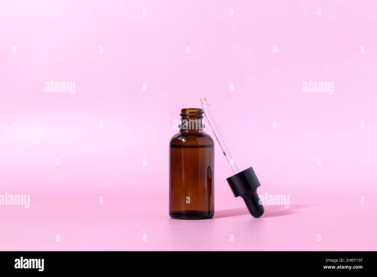 Flacon en verre brun avec compte-gouttes sur fond rose. Emballage de sérum ou d'huile essentielle. Maquette d'un produit cosmétique. Vue de face avec espace de copie. Banque D'Images