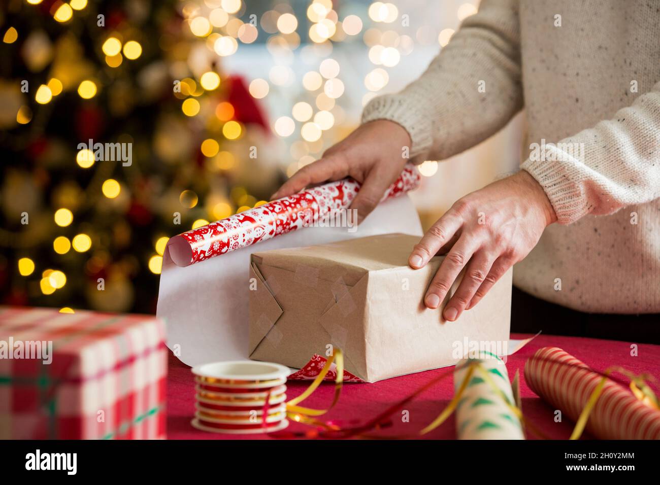 Homme et femme se préparant pour Noël.Couple de chandails chauds emballage cadeaux.Sapin de Noël décoré, boîtes avec cadeaux, papier d'emballage coloré Banque D'Images