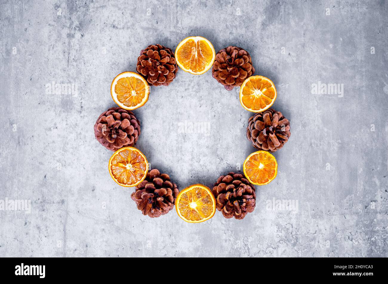 Couronne de Noël moderne ou couronne de l'Avent aux couleurs vives : tranches d'orange séchées alternant avec des cônes de pin sur un fond de couleur béton. Banque D'Images