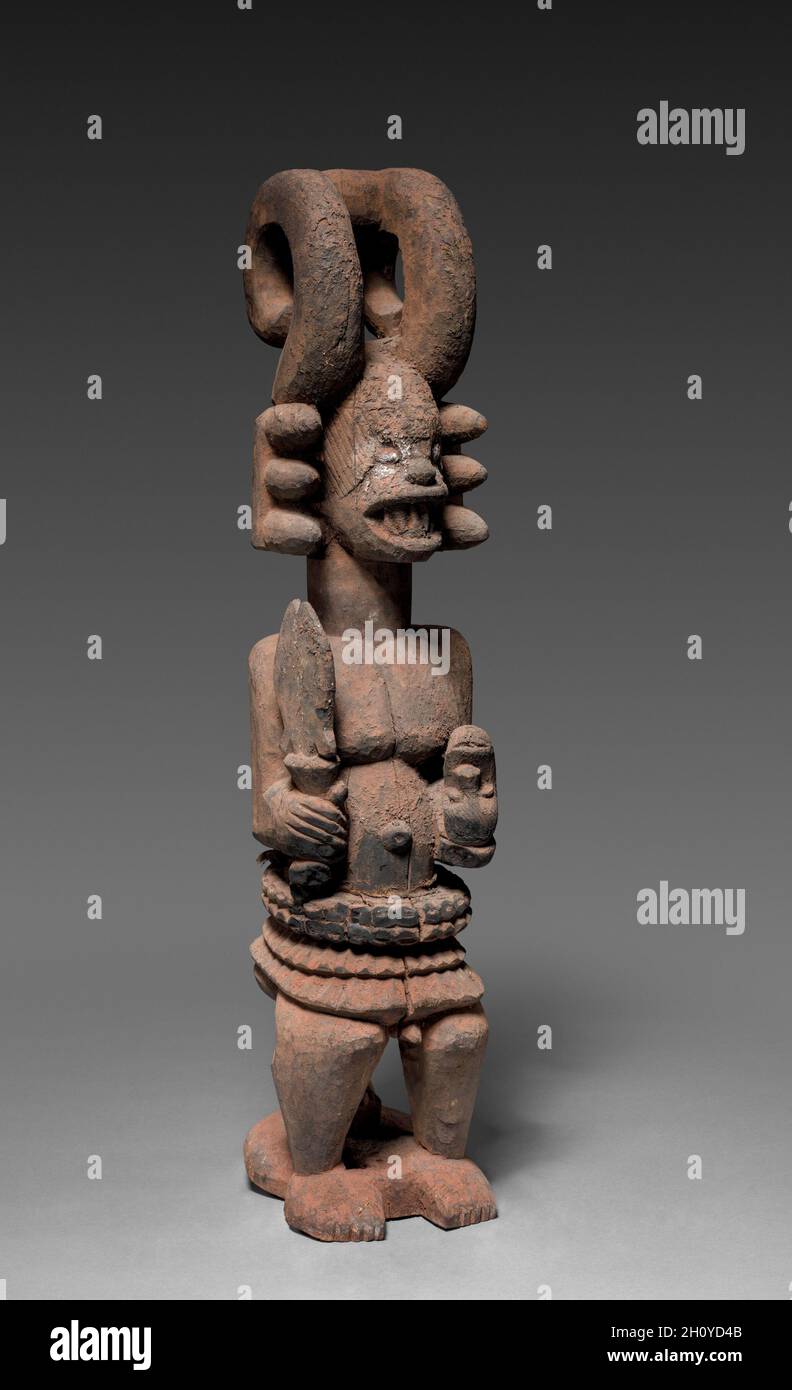 Figurine de sanctuaire (Ikenga), probablement au début des années 1900.Afrique, Afrique de l'Ouest, Nigeria, Igbo Carver.Bois, matières organiques et raphia; total: 74.5 x 18 x 20 cm (29 5/16 x 7 1/16 x 7 7/8 po).Cette figure assise d'un homme tenant un cutlass et un crâne humain inversé est un objet culte appelé ikenga, associé à la réalisation et au succès.Debout au centre du sanctuaire personnel d’un homme, la sculpture reçoit des prières et des sacrifices en échange de l’orientation des ancêtres.Une adresse élaborée comprenant deux extensions en forme de corne renforce la préoccupation du culte par rapport à la masculinité, tandis que l’incis faciale Banque D'Images