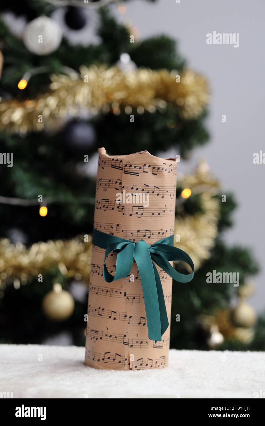 Magnifique cadeau de Noël décoré de musique et de notes sur le thème du  papier et du ruban de satin vert.Le présent a été photographié avec un  arbre de Noël Photo Stock -