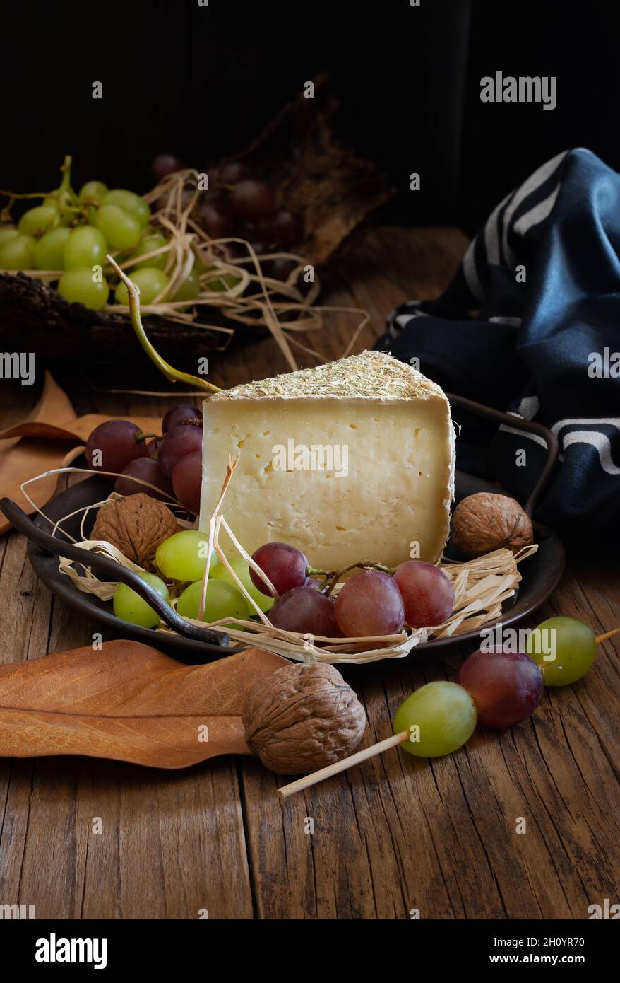 tranche de fromage pecorino avec du foin de montagne, sur fond automnal avec des raisins noirs Banque D'Images